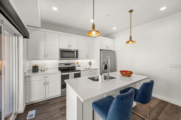 Modern kitchen featuring white cabinetry, stone countertops, stainless steel appliances, a center island with an integrated sink, and wood-finish flooring