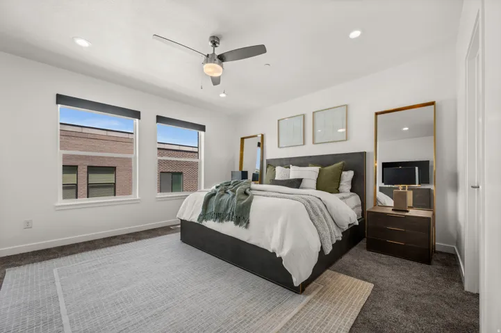 Spacious bedroom featuring dual windows with dark roller shades, a ceiling fan with integrated lighting, recessed lighting, and soft carpeting
