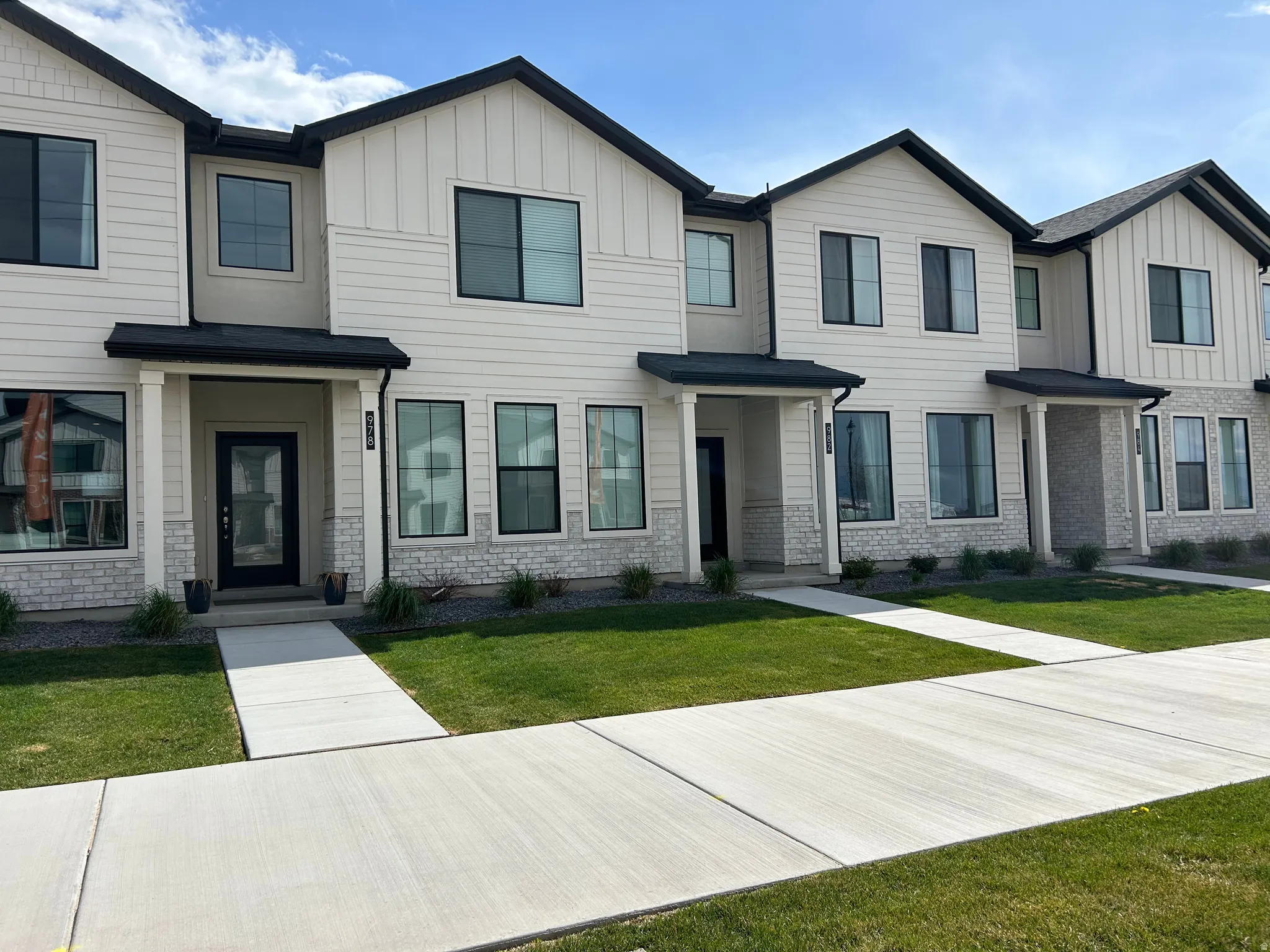 Modern townhome facade featuring white vertical and horizontal siding, black-framed windows, and stone veneer accents