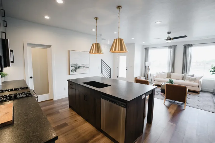 Open-concept living space featuring a central kitchen island with integrated sink, stainless steel dishwasher, and two brass pendant lights