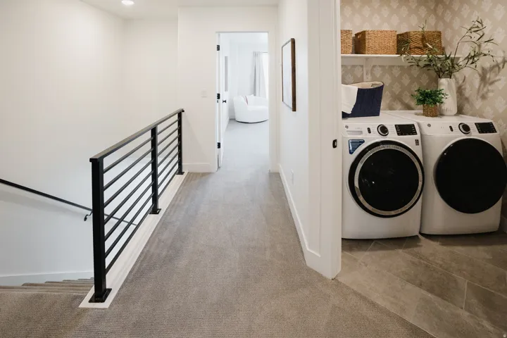 Dedicated laundry area featuring front-loading appliances, open shelving, and a patterned wall accent