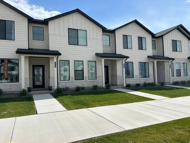 Modern townhome facade featuring white vertical and horizontal siding, black-framed windows, and stone veneer accents