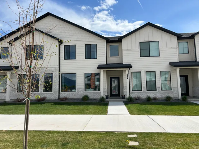 Contemporary townhome exterior featuring light-toned siding, black-framed windows, dark rooflines, stone-look accents, and a concrete walkway