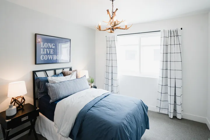 Bright bedroom featuring a large window, antler-style chandelier, and carpeted flooring