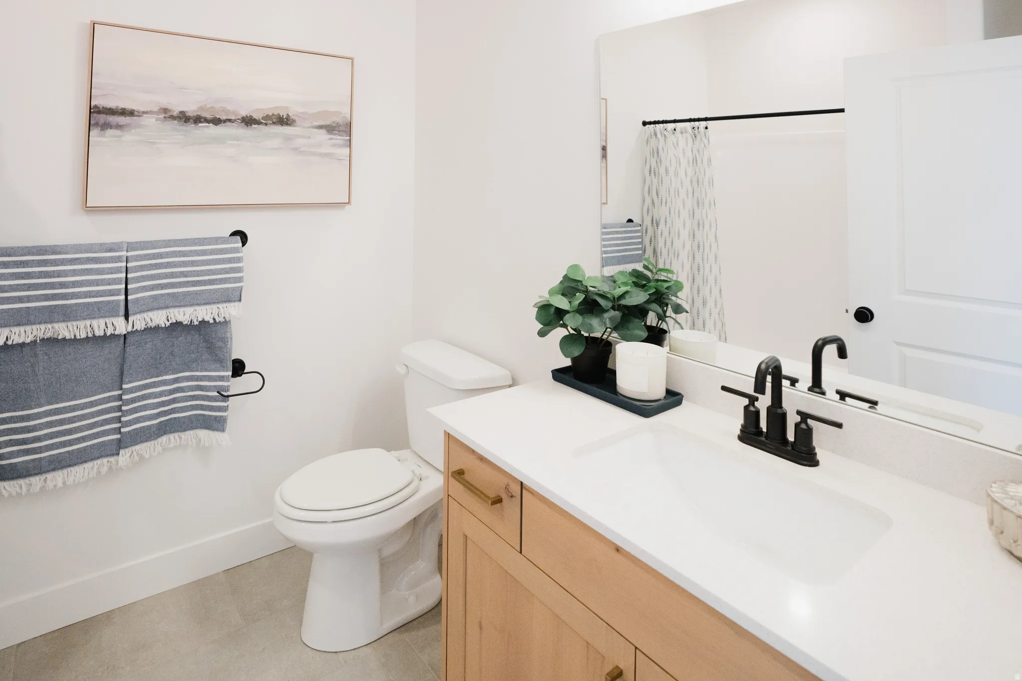 Bathroom vanity featuring light wood-finish cabinetry with brass hardware, a white countertop with an integrated sink, and a matte black faucet