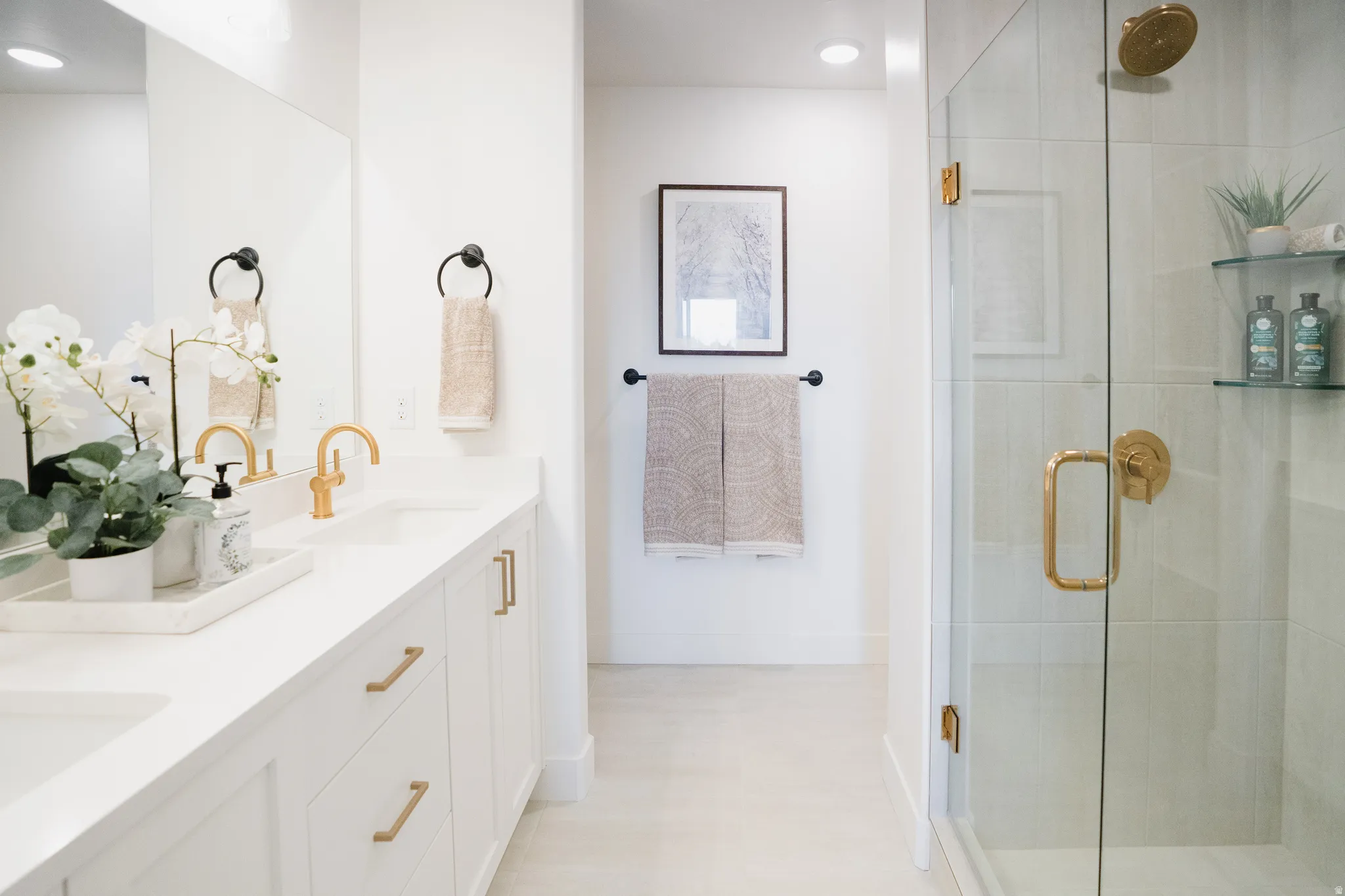 Bathroom featuring a double vanity with white cabinetry and integrated sinks, brushed gold faucets, and a glass-enclosed shower with gold-tone fixtures