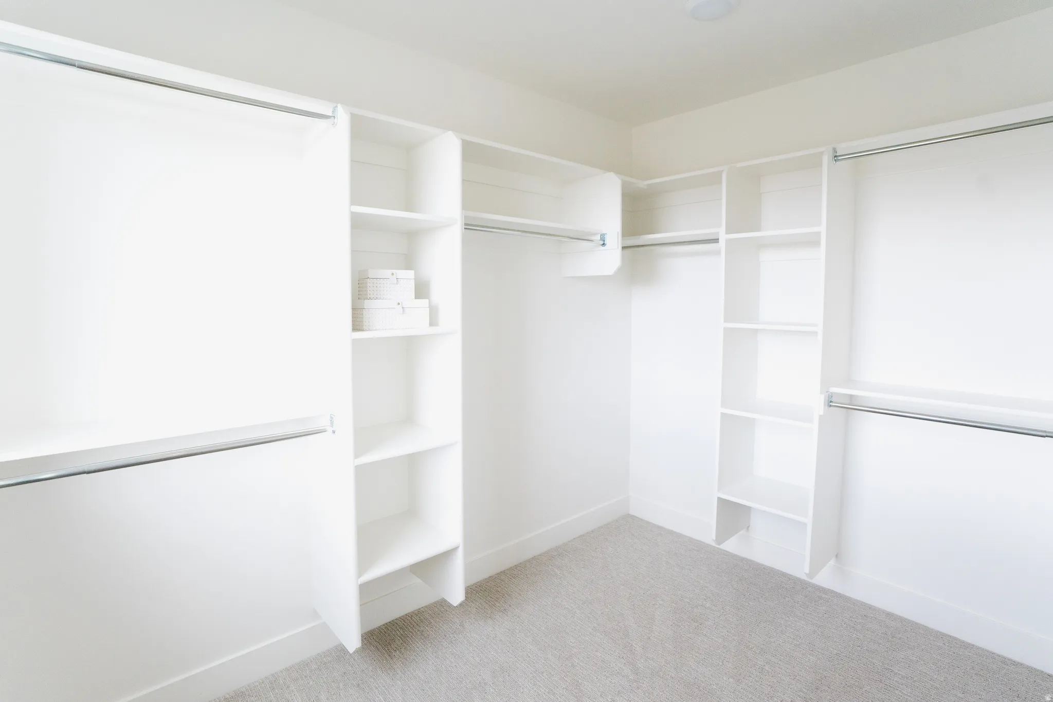 Custom closet system featuring white shelving units, multiple hanging rods, and light gray carpet
