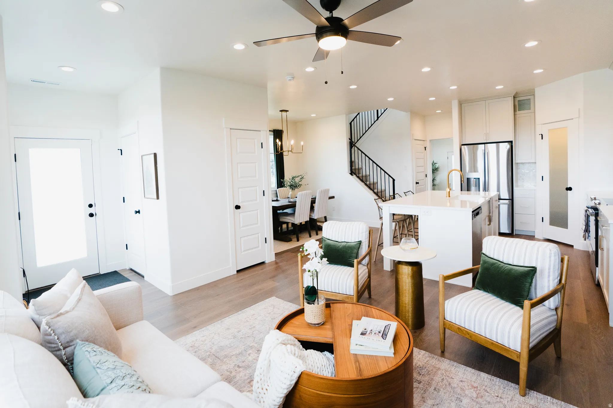 Open-concept living space featuring wood-finish flooring, recessed lighting, a ceiling fan, a kitchen island with seating, and a modern stair railing