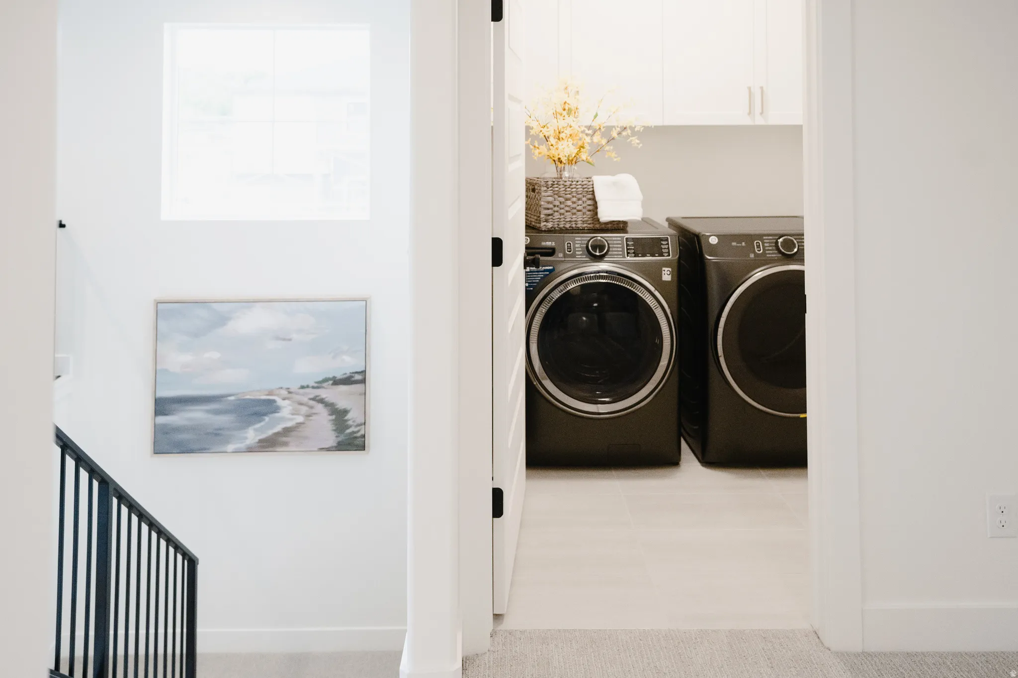Dedicated laundry area featuring front-loading appliances, white cabinetry, and light-toned tile flooring