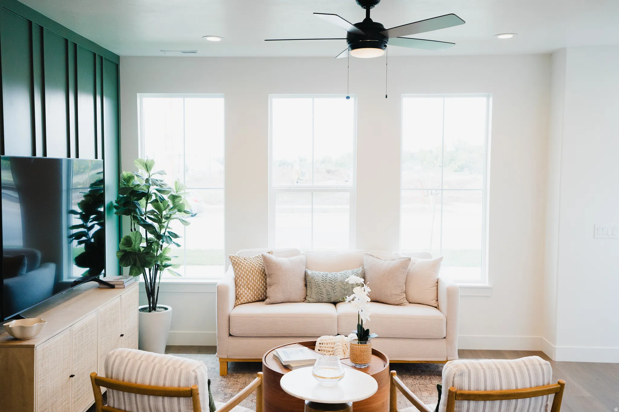 Living area featuring three large windows, a black ceiling fan with integrated lighting, recessed lighting, and a prominent accent wall with vertical paneling