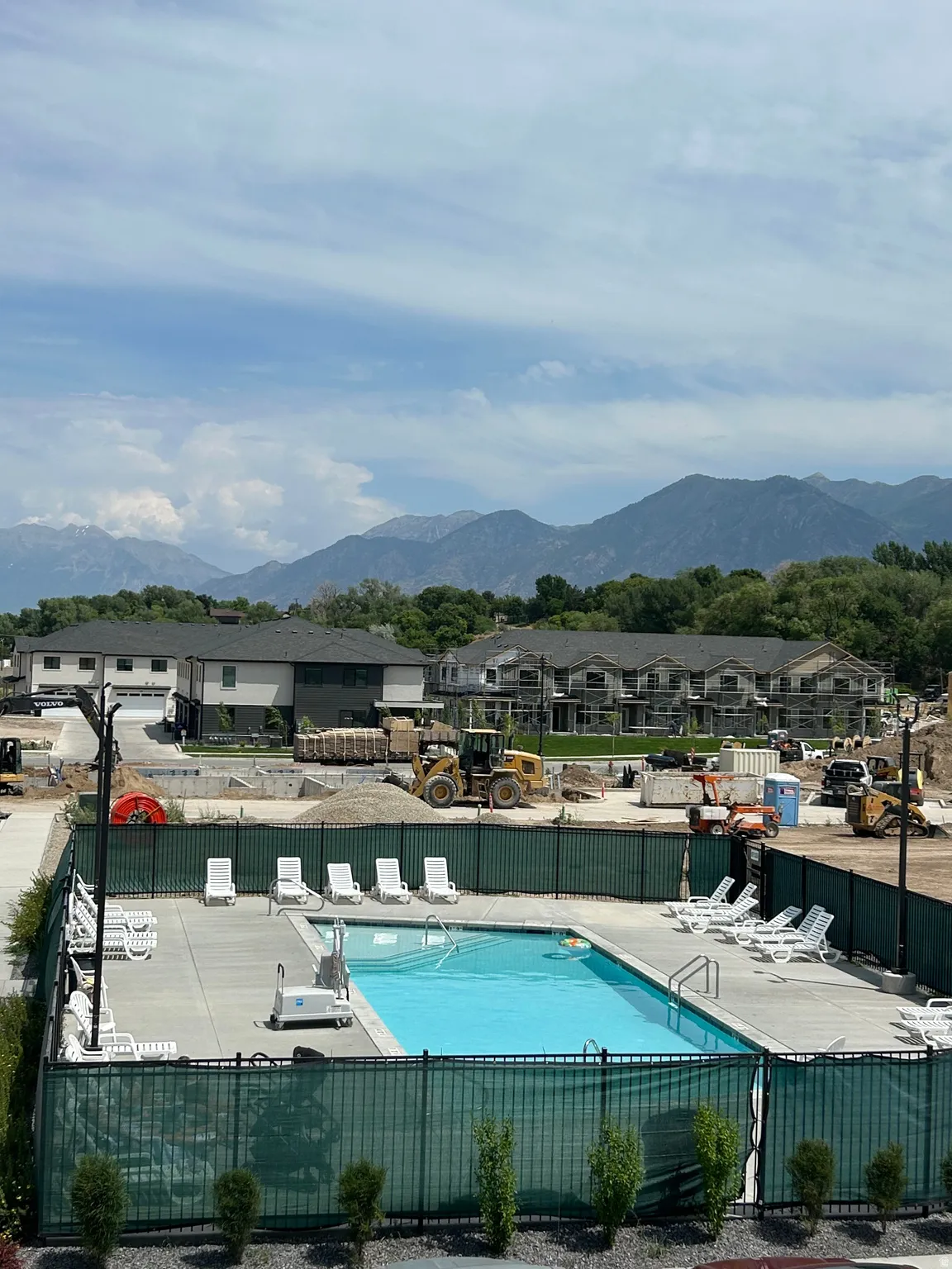 Outdoor swimming pool with concrete decking, surrounded by a metal fence with privacy screening, and framed by distant mountains