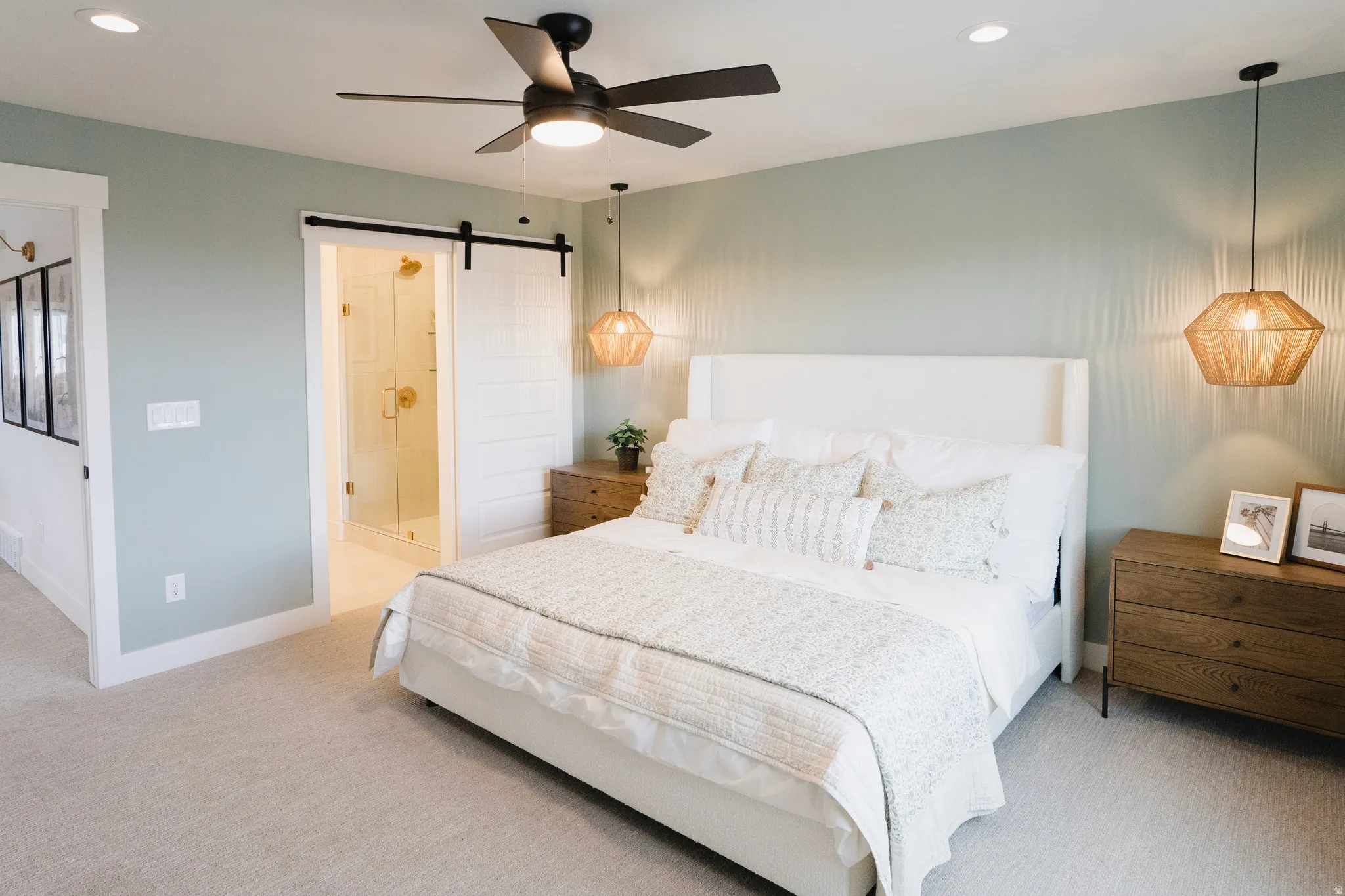 Spacious room featuring light-colored carpet flooring, a barn door entry to an adjoining bath, a glass-enclosed shower, a ceiling fan with integrated lighting, and recessed ceiling lights