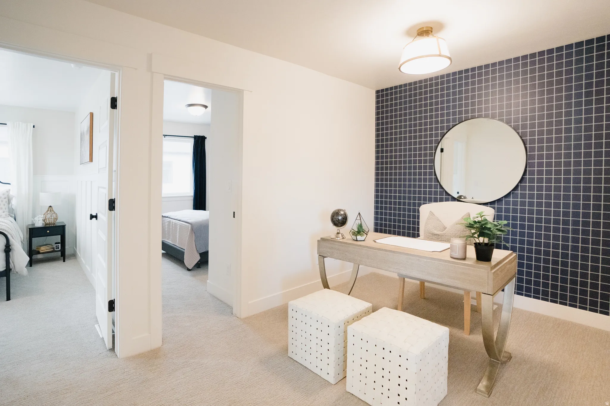 Carpeted room featuring a grid-pattern accent wall, a circular black-framed mirror, and a semi-flush mount ceiling light