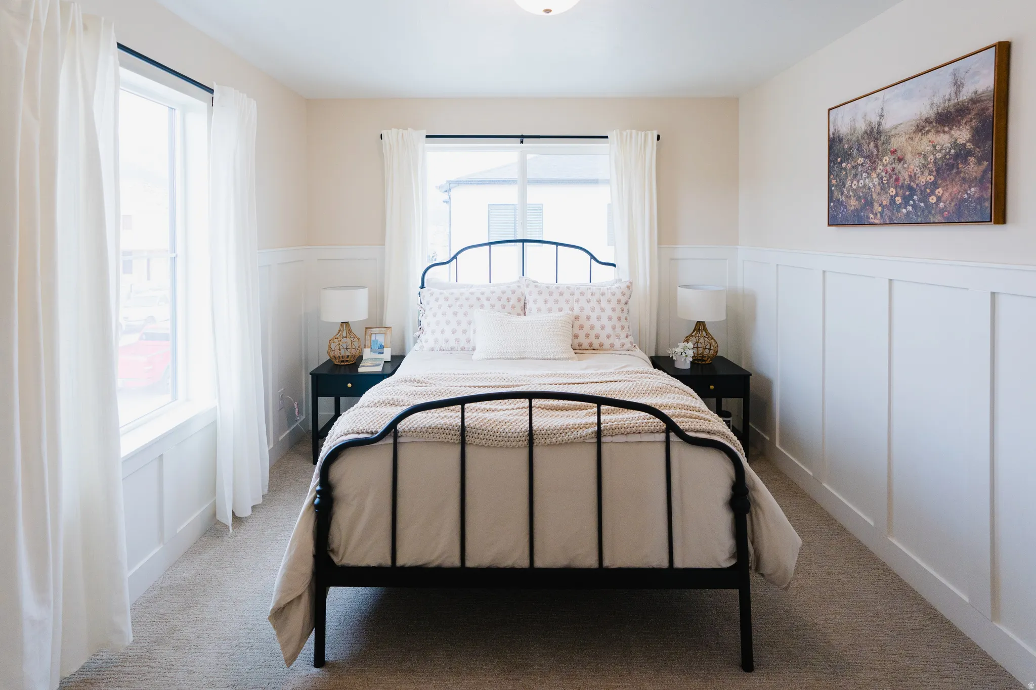Bedroom featuring extensive wainscoting on all walls, dual windows with black trim, and carpeted flooring