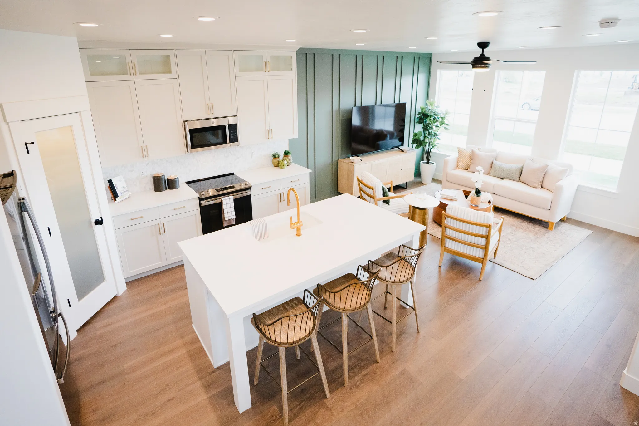 Open-concept living space featuring wood-finish flooring, a kitchen island with seating, white cabinetry, stainless steel appliances, and large windows