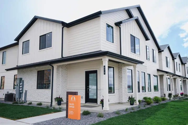 Contemporary townhome exterior featuring white vertical and horizontal siding, black-framed windows, white brick accents, and a covered porch entry