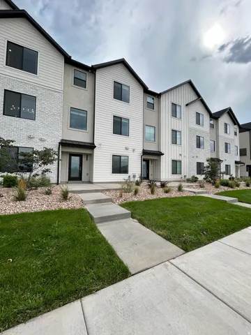 Contemporary townhouse exterior with white vertical siding, light-colored stone accents, dark-framed windows, a concrete walkway, and landscaped front yard