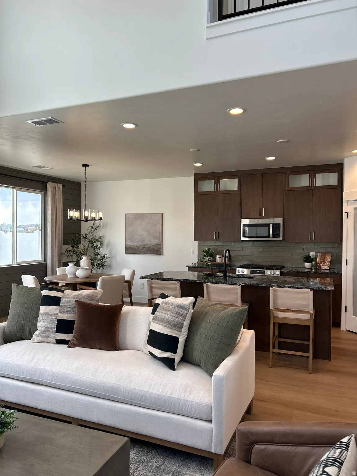 Open-concept living space featuring high ceilings, recessed lighting, wood-finish flooring, a kitchen island with seating, and dark wood cabinetry