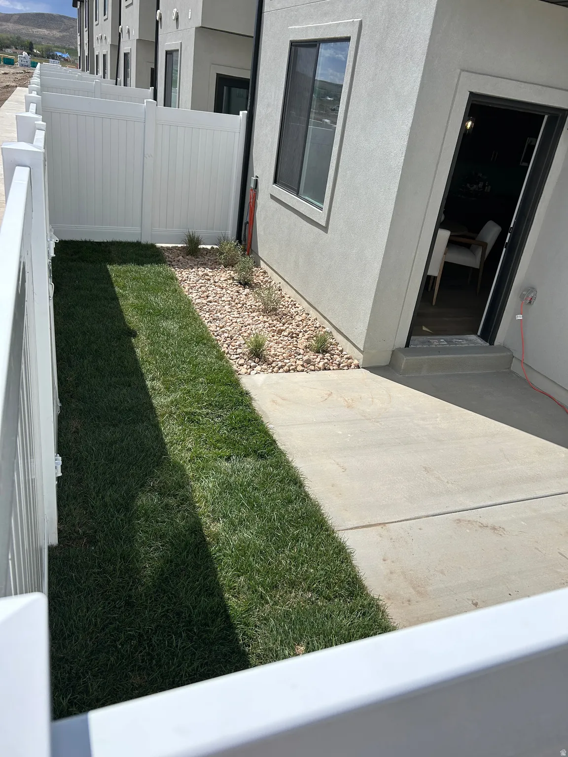 Private outdoor patio area featuring a concrete slab, a strip of green lawn, and a rock garden with small plantings