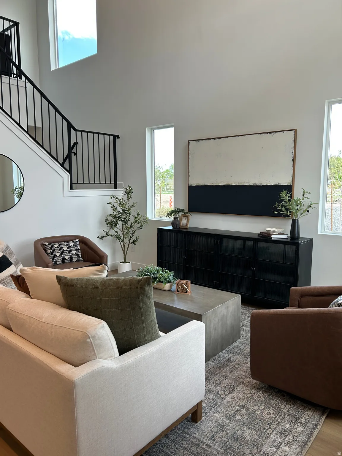 Open-concept living space featuring high ceilings, contemporary black metal stair railings, and tall rectangular windows