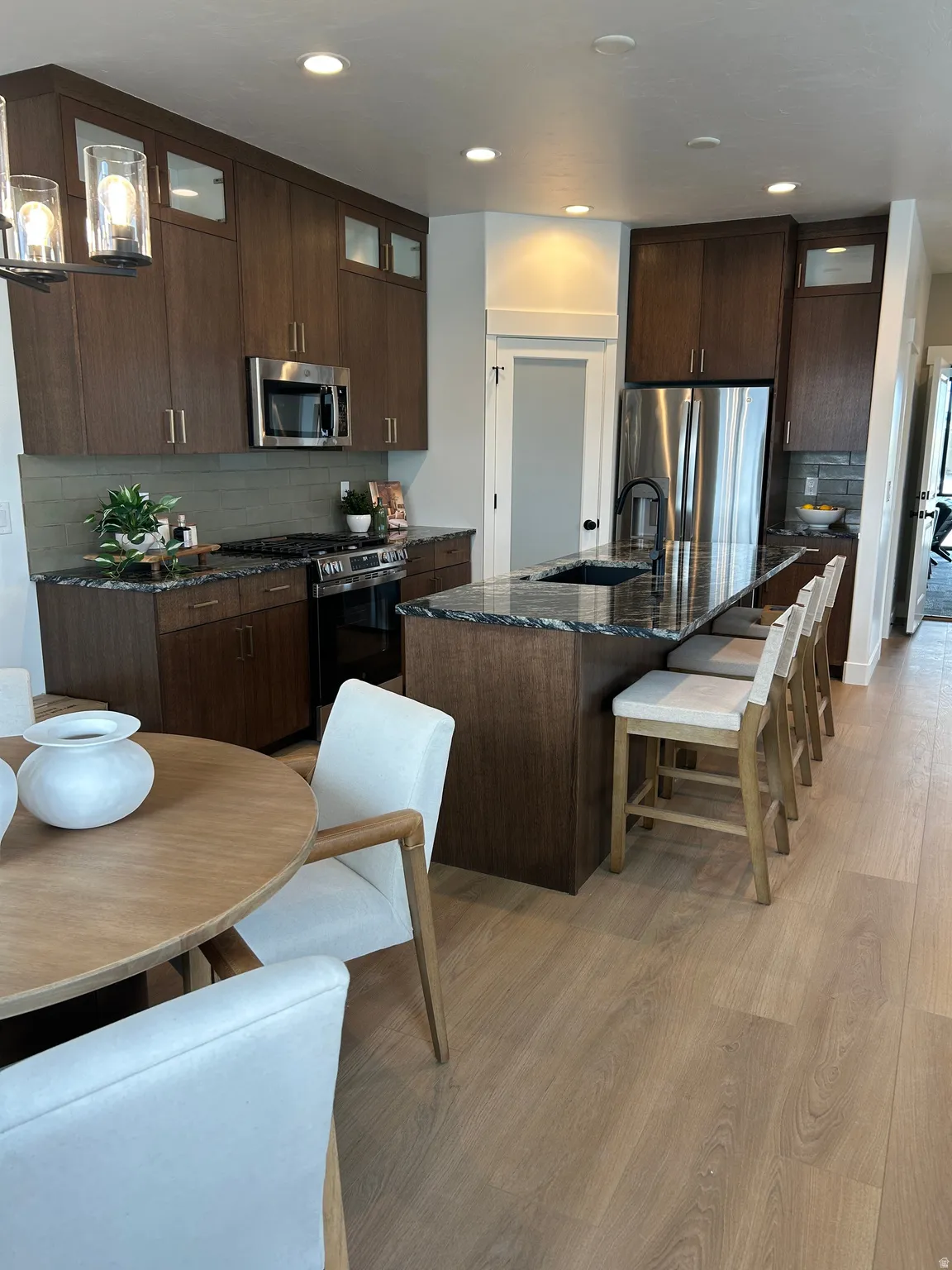 Modern kitchen featuring dark wood-finish cabinetry, stainless steel appliances, a spacious island with a sink, and light wood-finish flooring