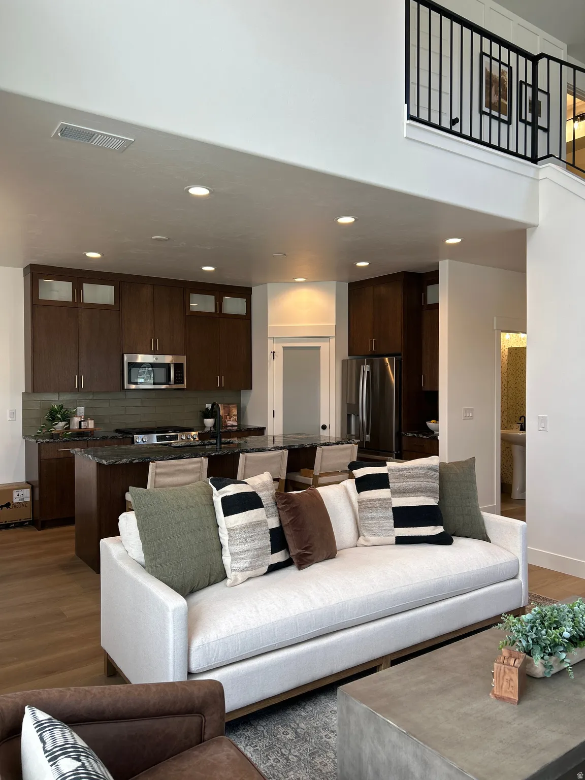 Open-concept living area featuring high ceilings, wood-finish flooring, a kitchen island with seating, dark wood cabinetry, and stainless steel appliances