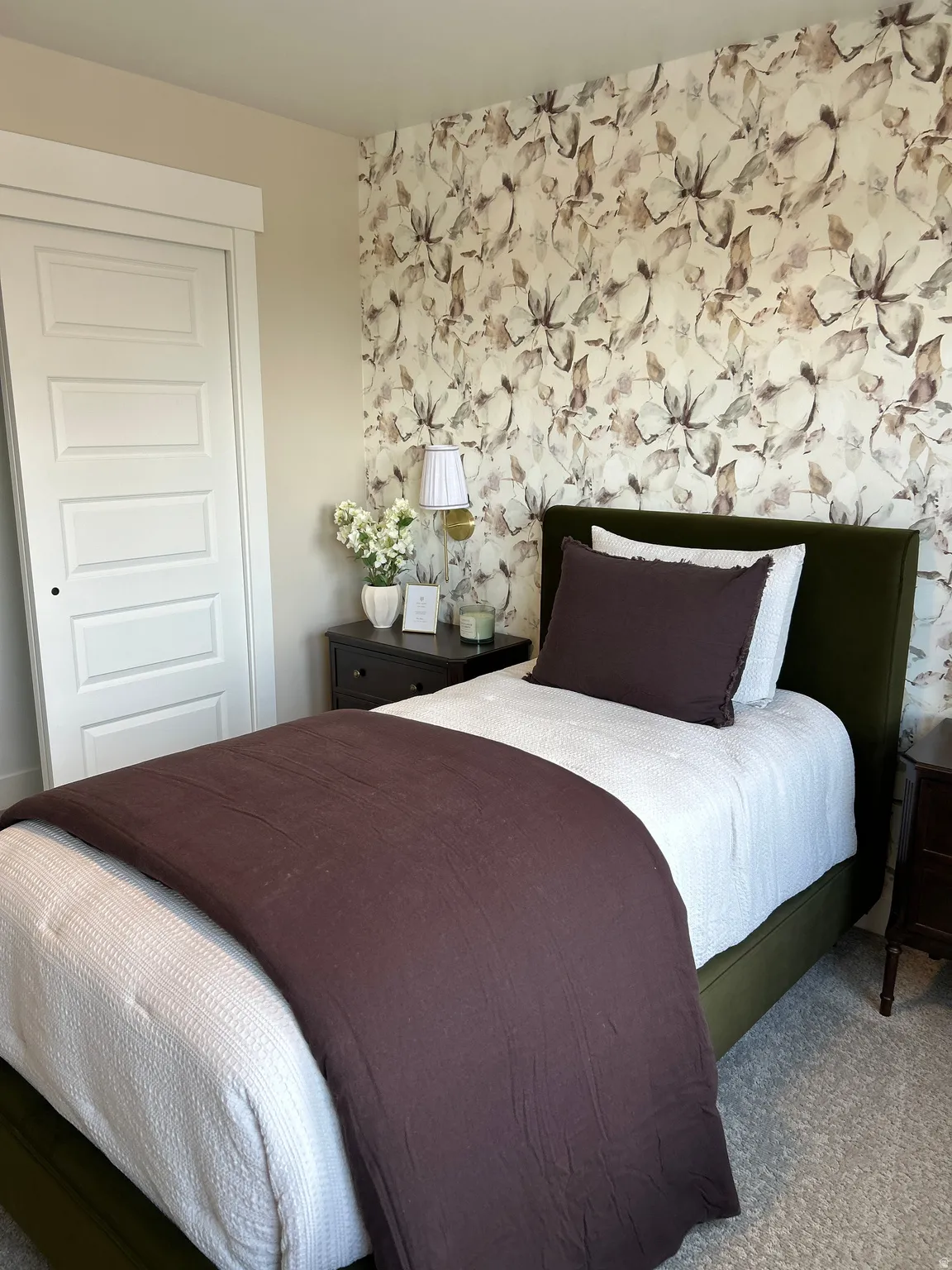 Bedroom featuring a patterned accent wall, light-colored carpeting, a sliding closet door, and painted baseboards