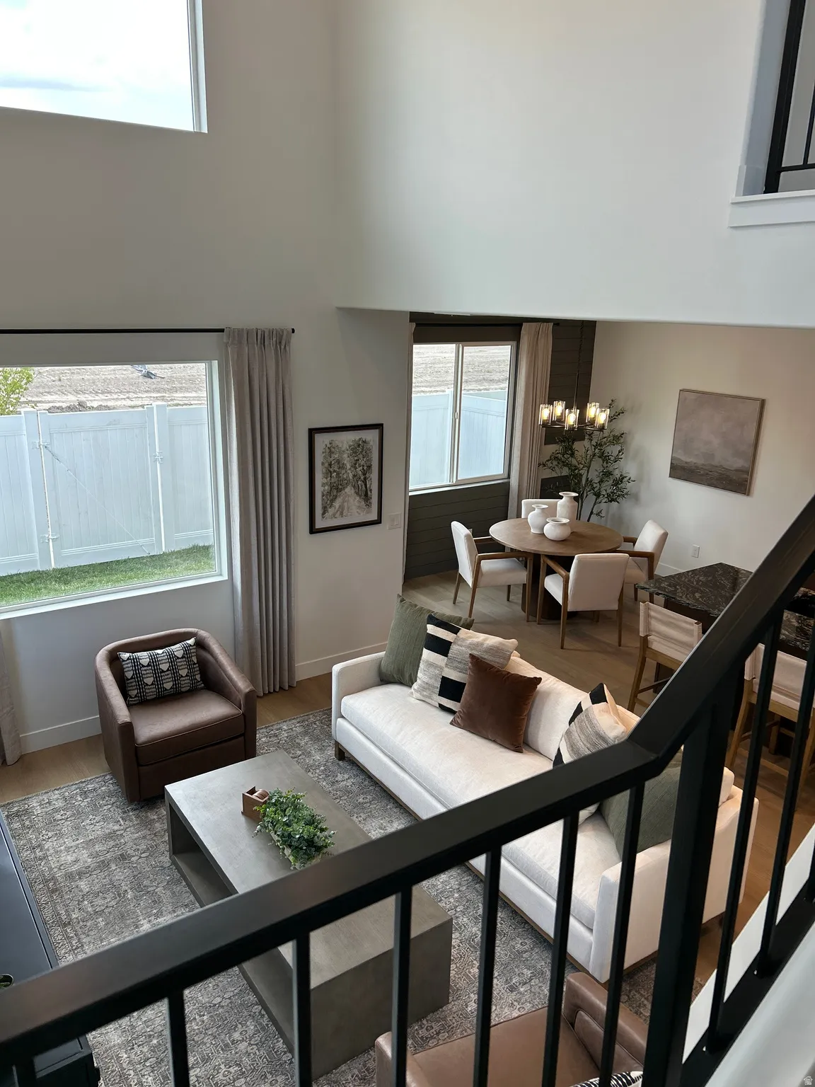 Open-concept living space featuring high ceilings, wood-finish flooring, a contemporary black metal railing, and abundant natural light from multiple windows