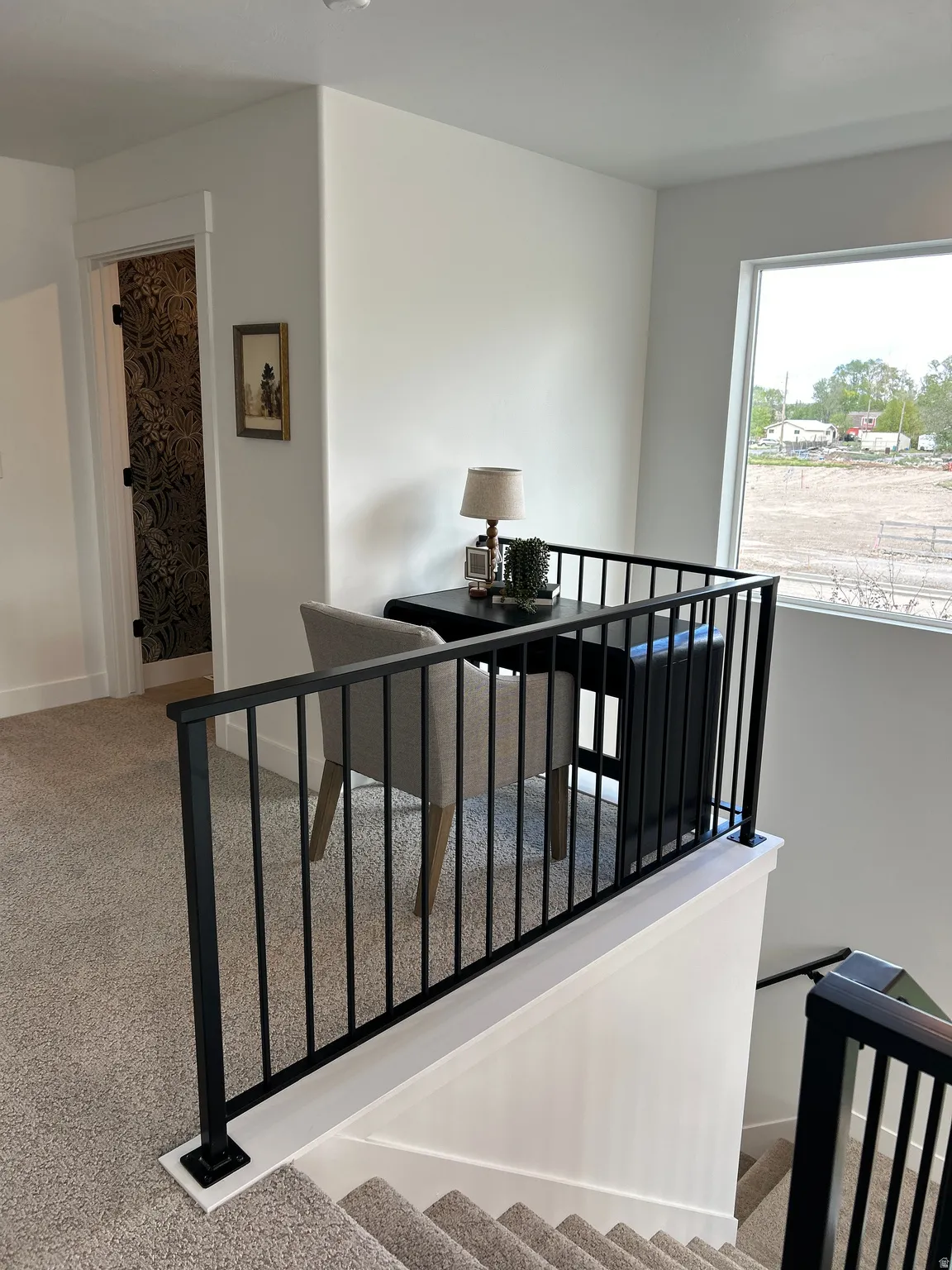 Upper-level landing featuring a contemporary black iron railing, neutral carpeted flooring, and a large window providing ample natural light