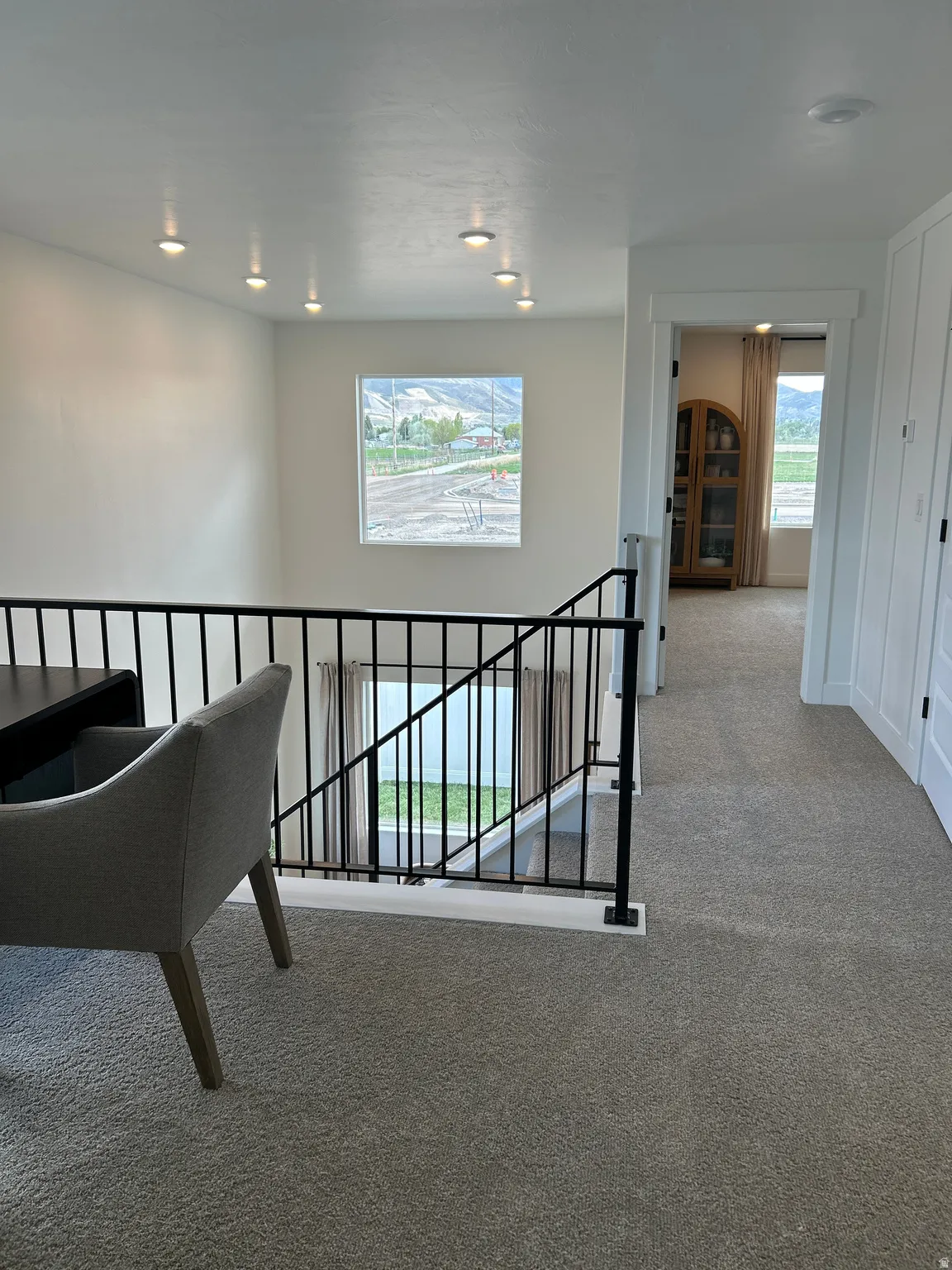 Carpeted upper landing featuring a black metal baluster railing system, recessed ceiling lighting, and a white framed window