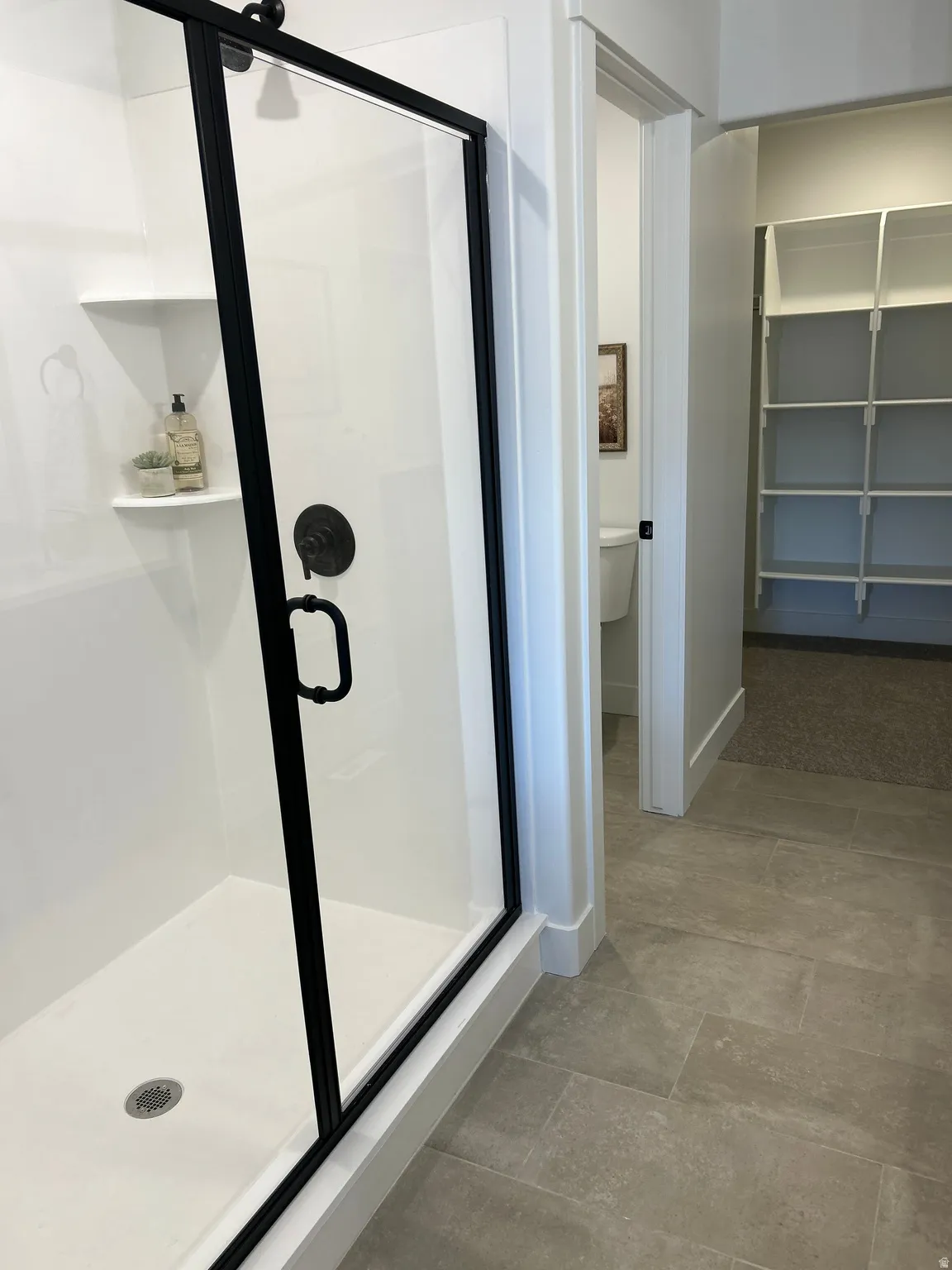 Contemporary shower enclosure featuring a frameless glass door with matte black trim, dark bronze fixtures, and integrated shelving