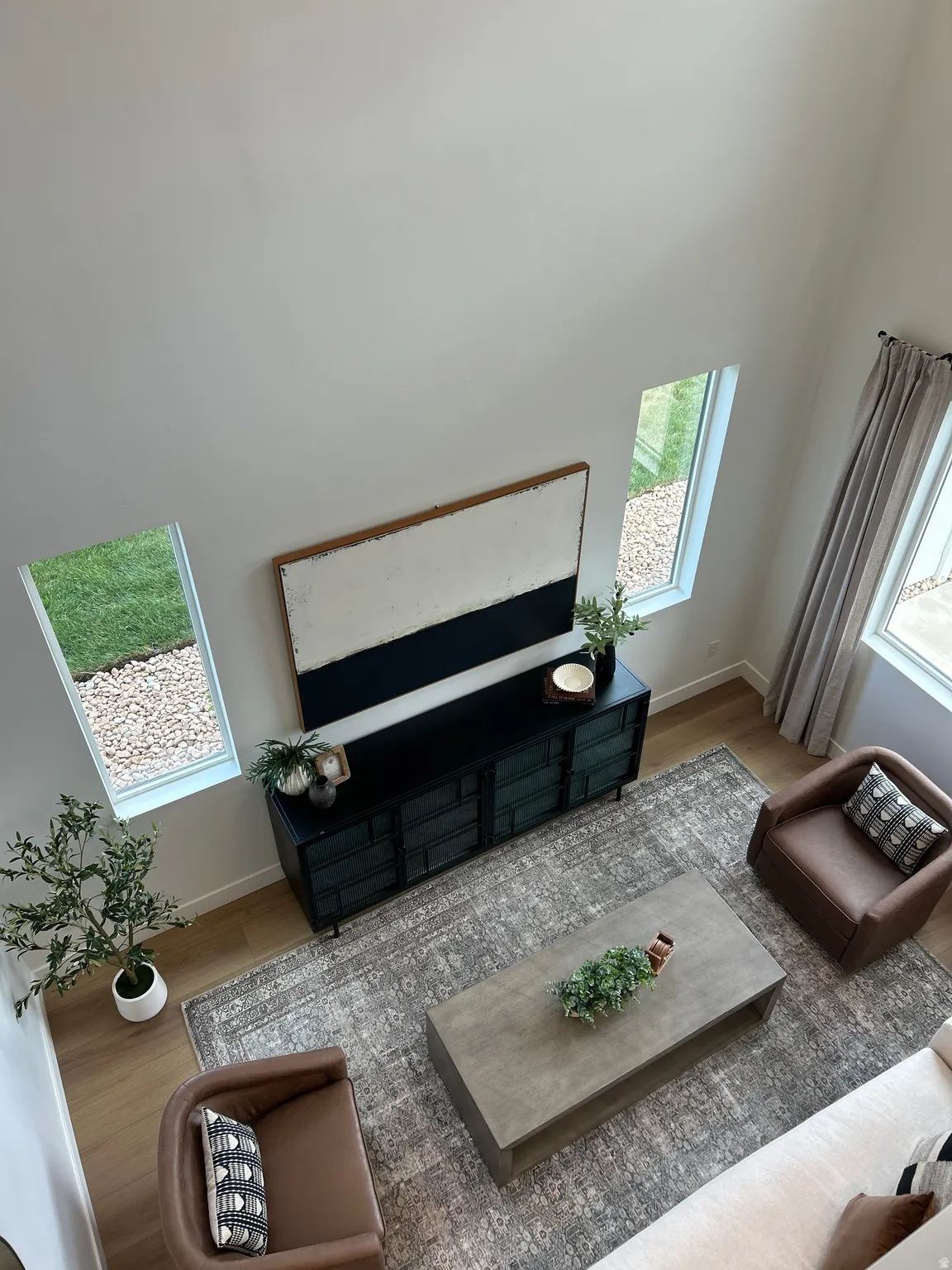 High ceilings with tall windows, light wood-finish flooring, and a patterned area rug define this living space