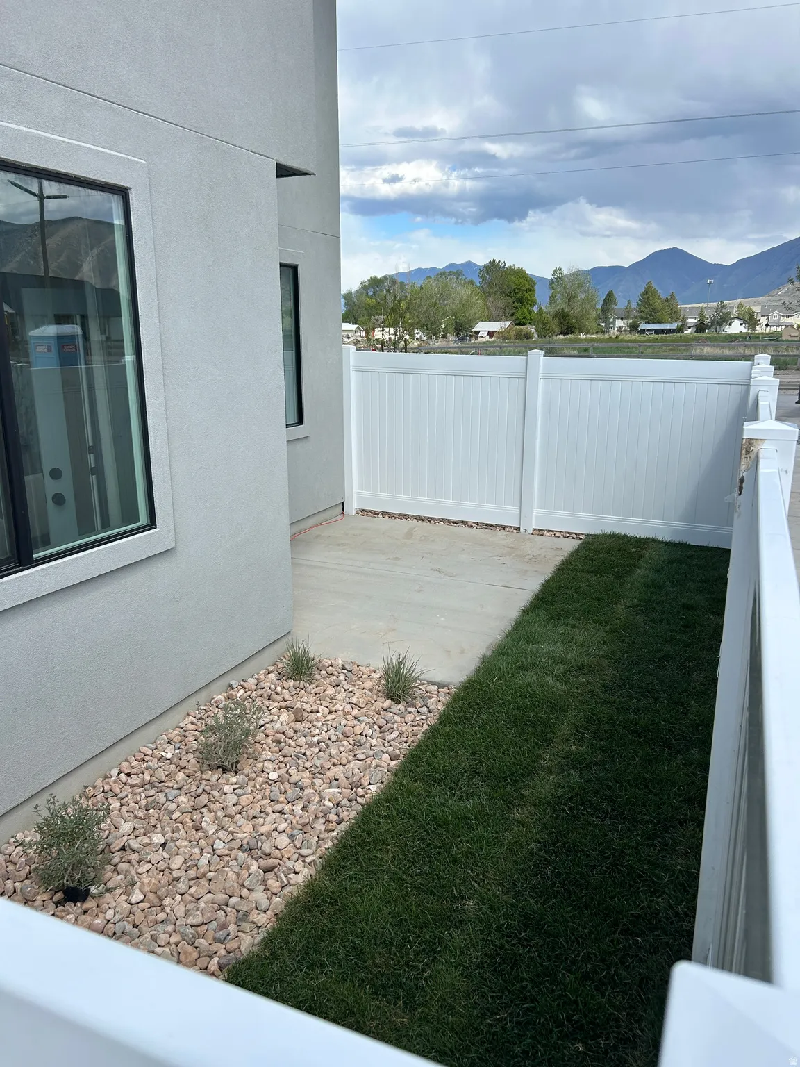 Private side yard with a white vinyl fence, concrete patio, and landscaped rock bed