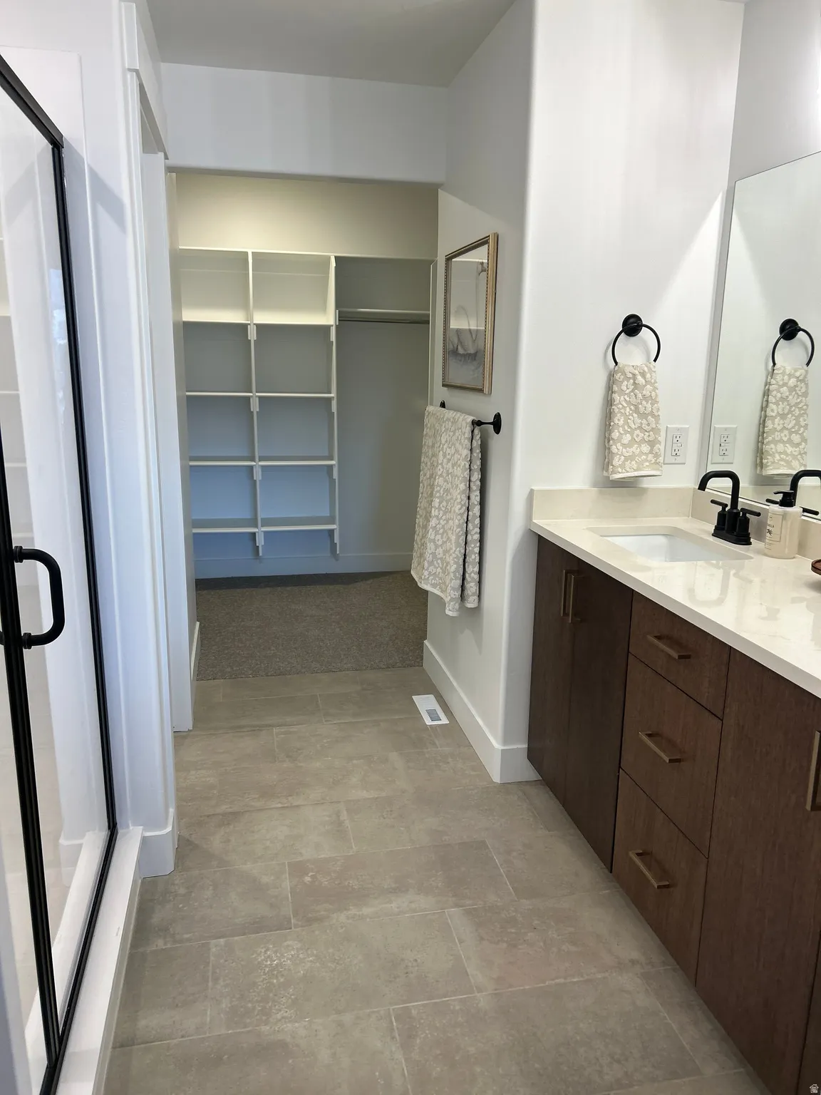 Bathroom featuring a dual vanity with wood-finish cabinetry, light-toned countertop, and matte black fixtures