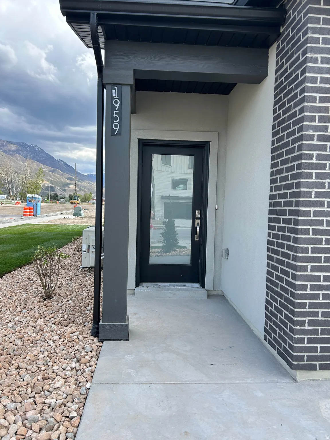 Modern entryway featuring a dark-framed glass door, concrete walkway, and gravel landscaping