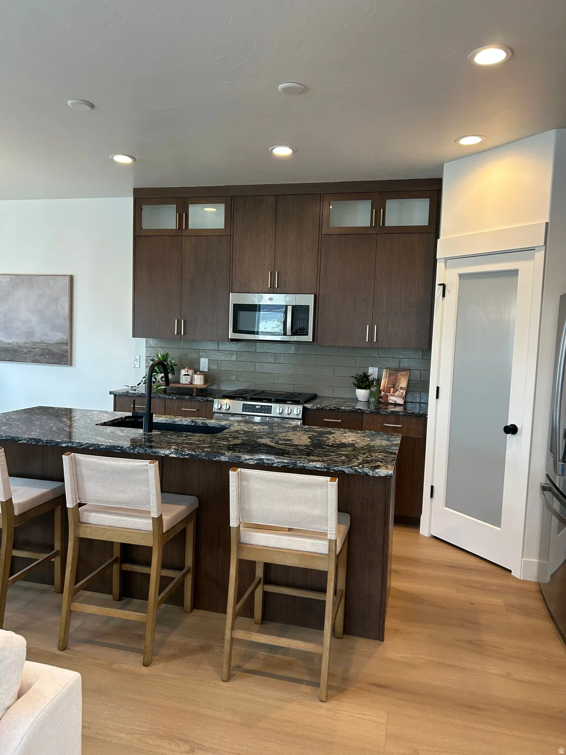 Gourmet kitchen featuring a large island with seating, stainless steel appliances, dark wood-finish cabinetry, and a frosted glass pantry door