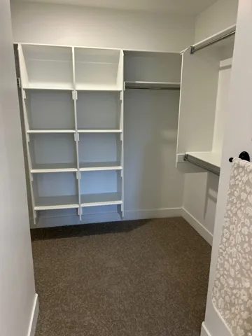 Walk-in closet featuring built-in white shelving, multiple hanging rods, and neutral-toned carpeting