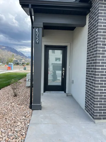 Modern entryway featuring a dark-framed glass door, concrete walkway, and gravel landscaping