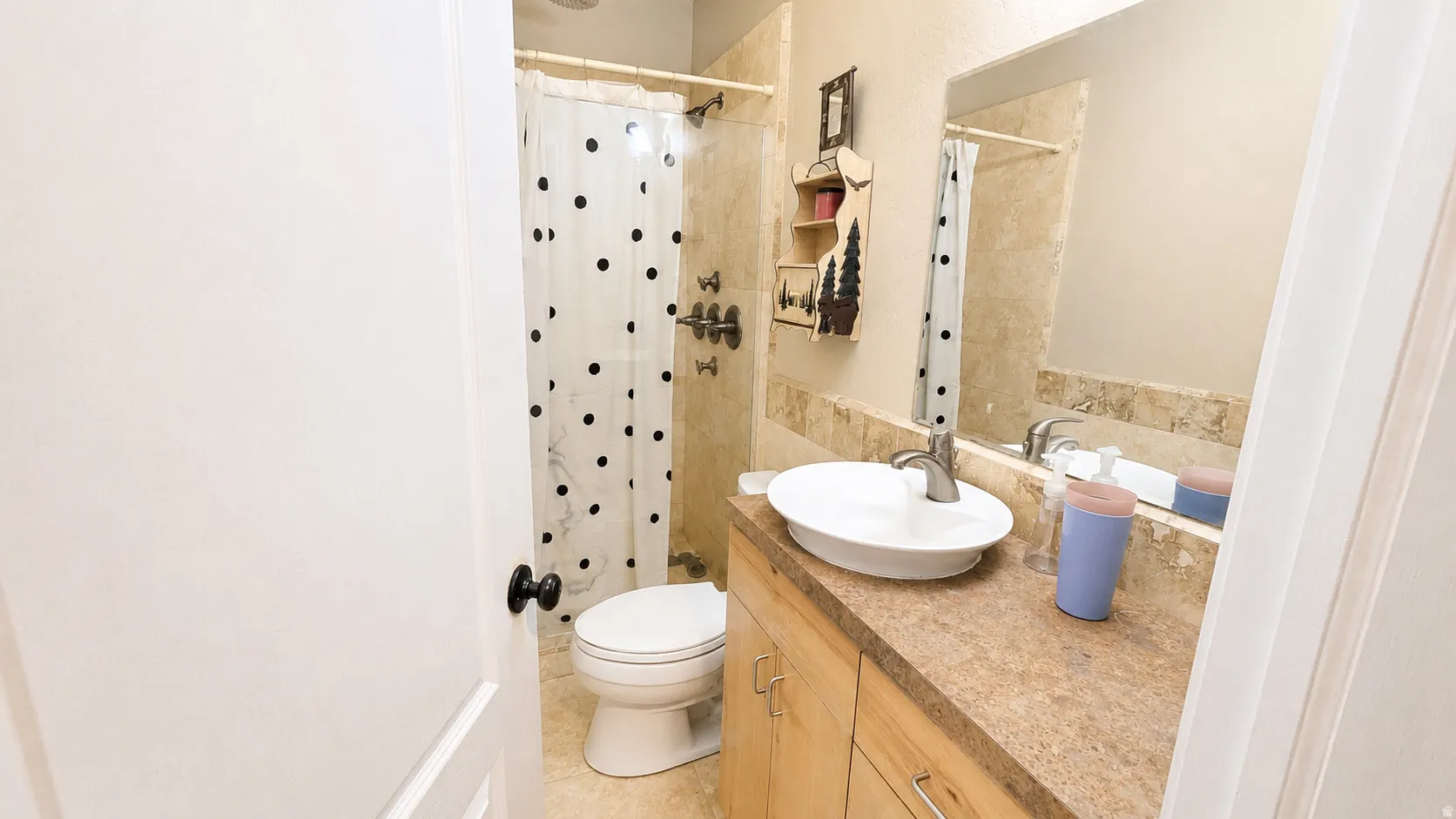 Bathroom featuring a vessel sink, wood-finish cabinetry, a large vanity mirror, and a shower with tile surround