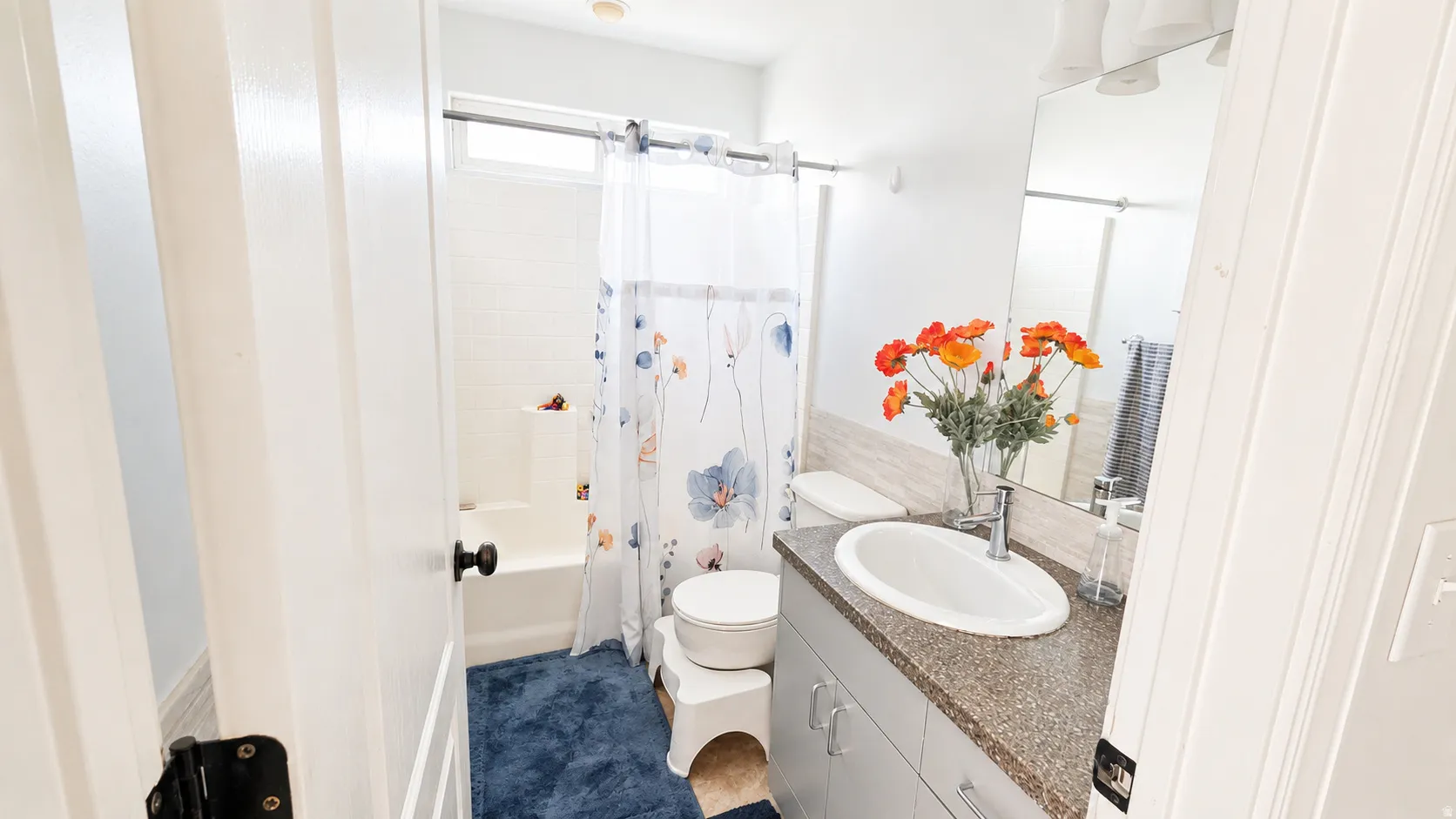 Bathroom featuring a white bathtub, a single vanity with an integrated sink, a speckled countertop, and a large wall-mounted mirror