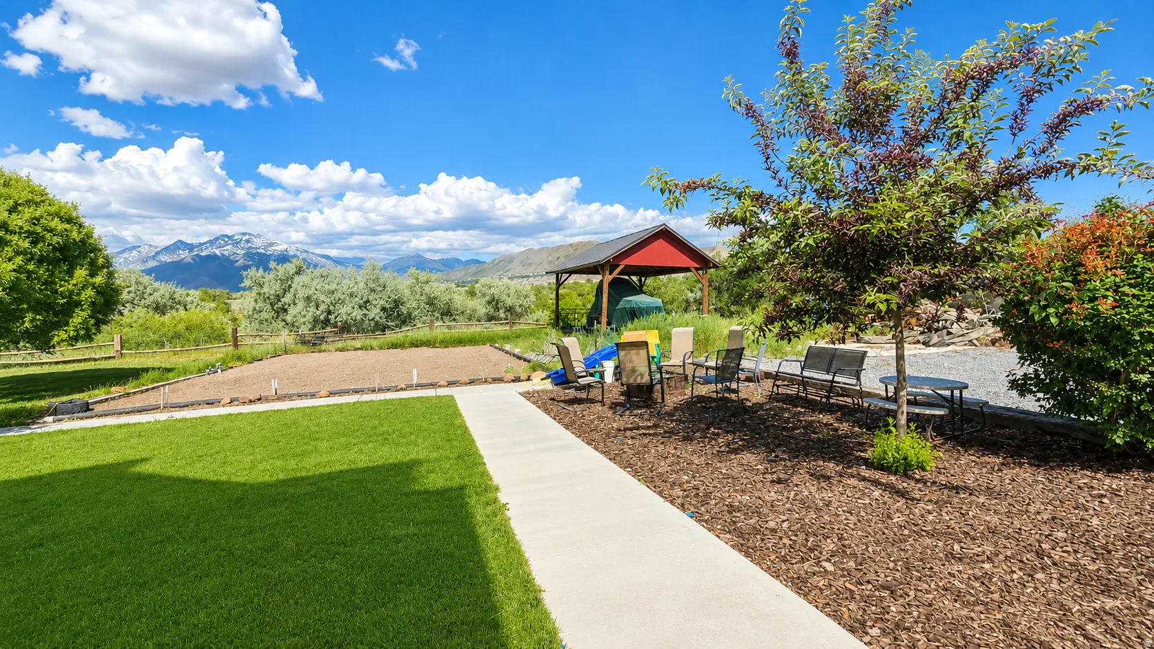 Expansive backyard featuring a manicured lawn, concrete pathway, and a covered patio area with a red roof