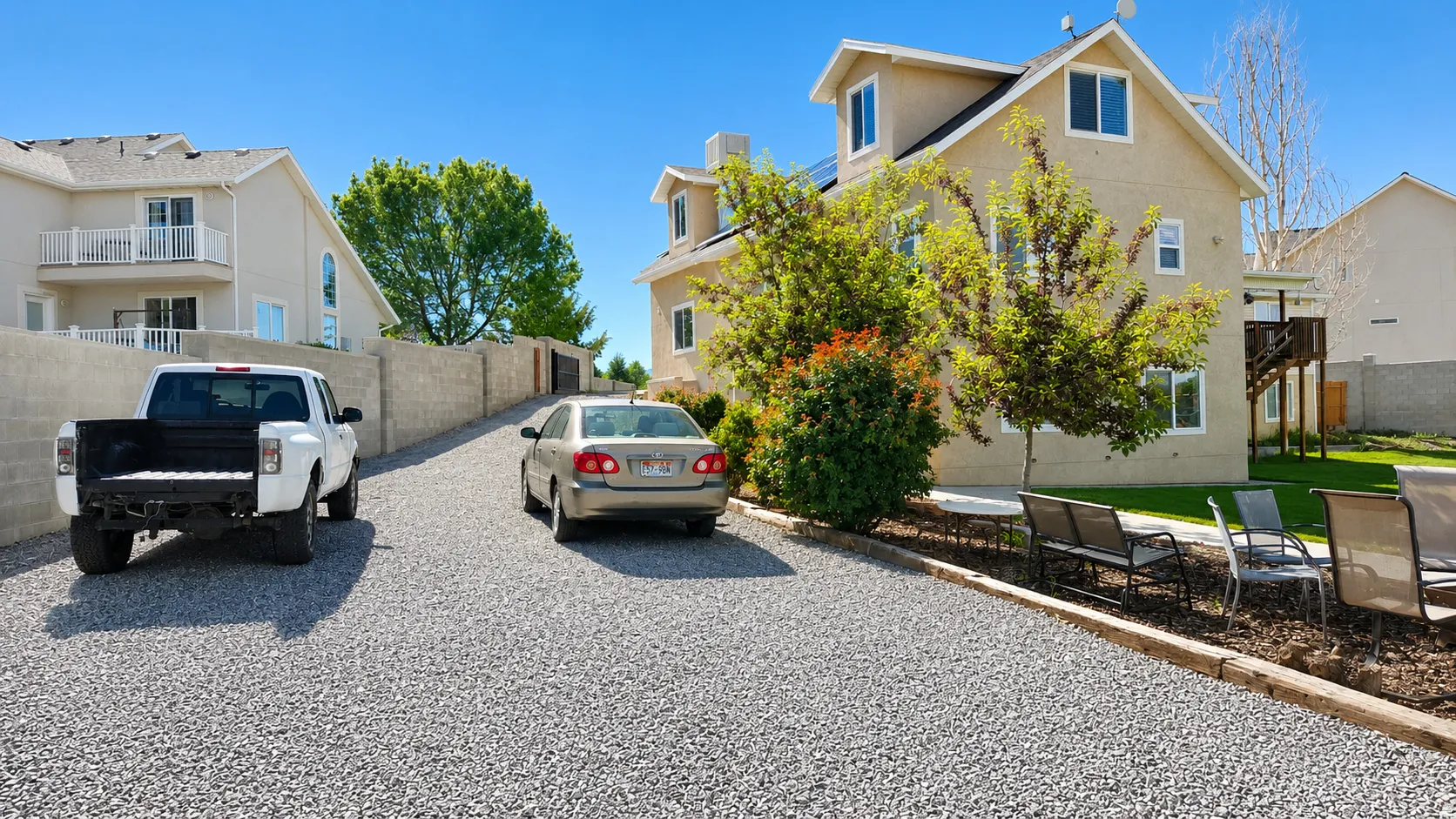 Spacious gravel driveway providing ample parking, bordered by a concrete block privacy wall and established landscaping