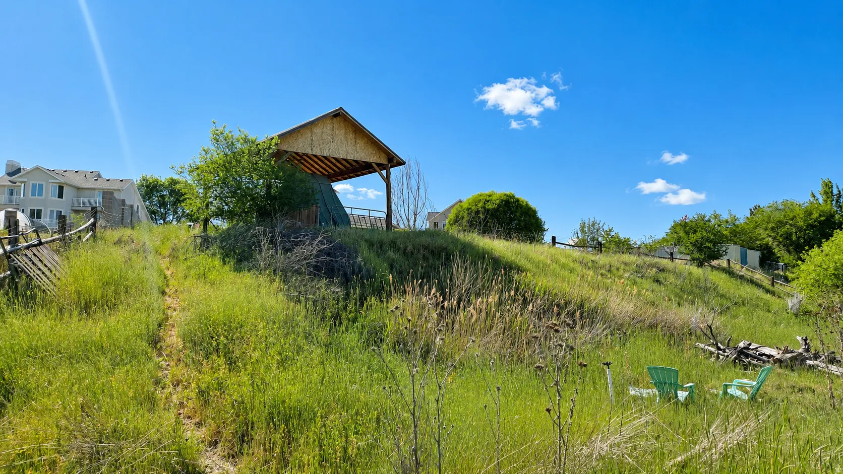 Expansive grassy hillside with a wooden pergola structure and split-rail fencing