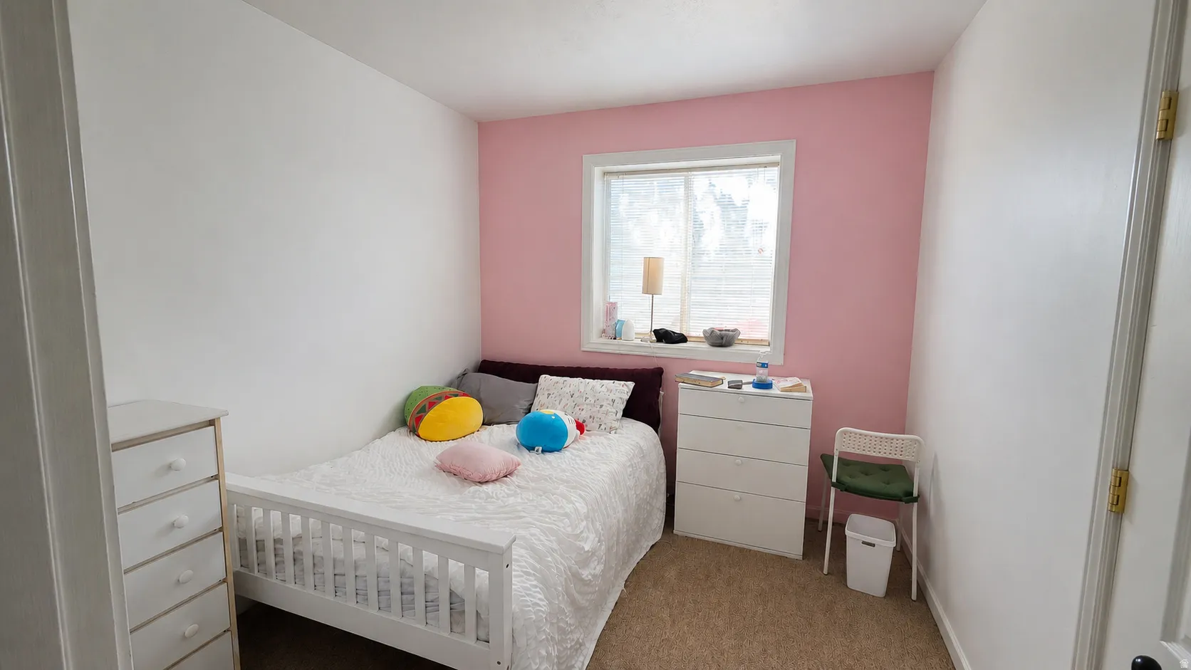 Bedroom featuring a window with white trim, a pink accent wall, and neutral carpeting