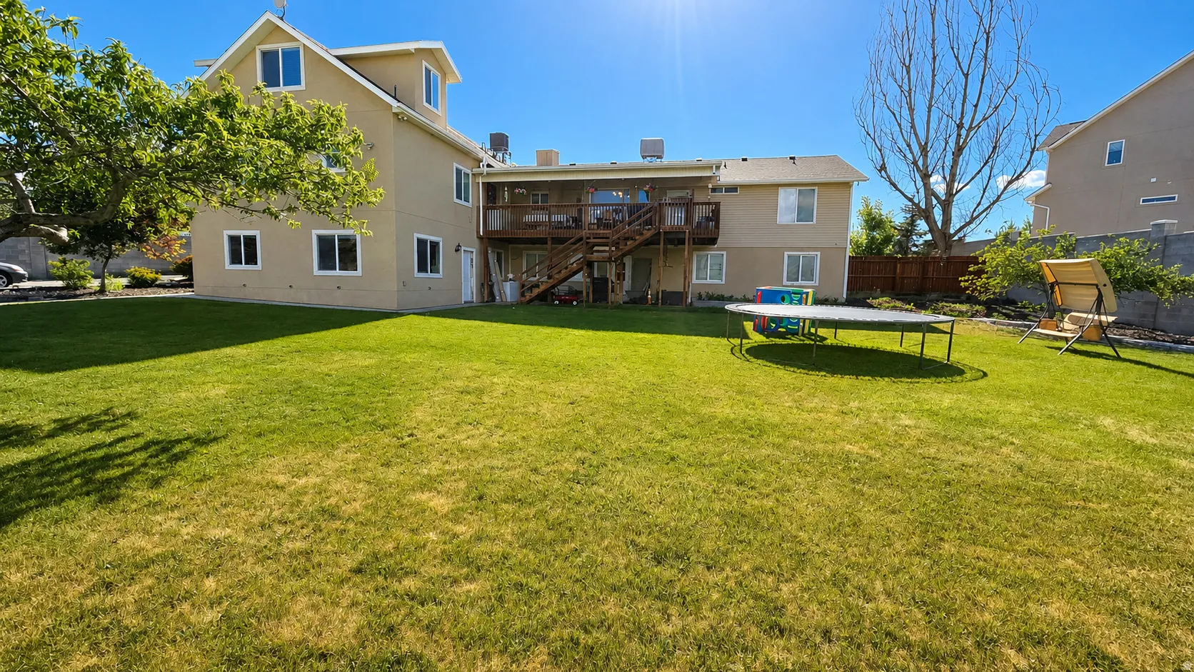 Expansive rear yard featuring a manicured lawn, multi-level deck with wood railing, and mature landscaping