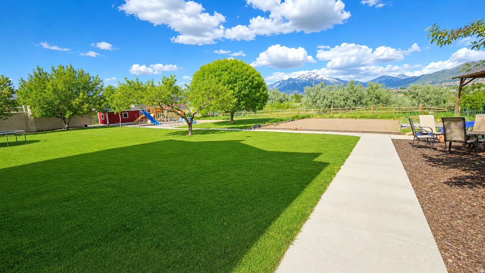 Expansive outdoor space featuring a broad lawn, mature trees, and a concrete pathway