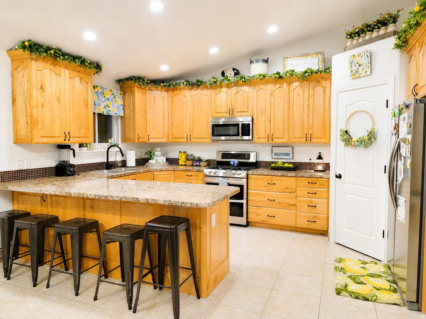 Kitchen featuring light wood cabinetry with black hardware, an integrated kitchen island with seating, stone-finish countertops, and stainless steel appliances