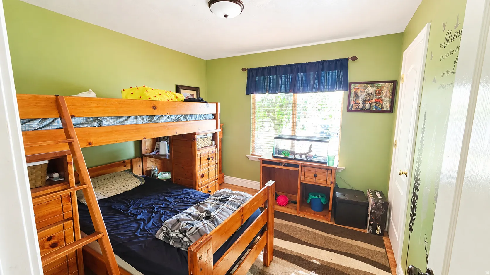 Bright room featuring a window with blinds, light green walls, a ceiling-mounted light fixture, and wood-finish flooring