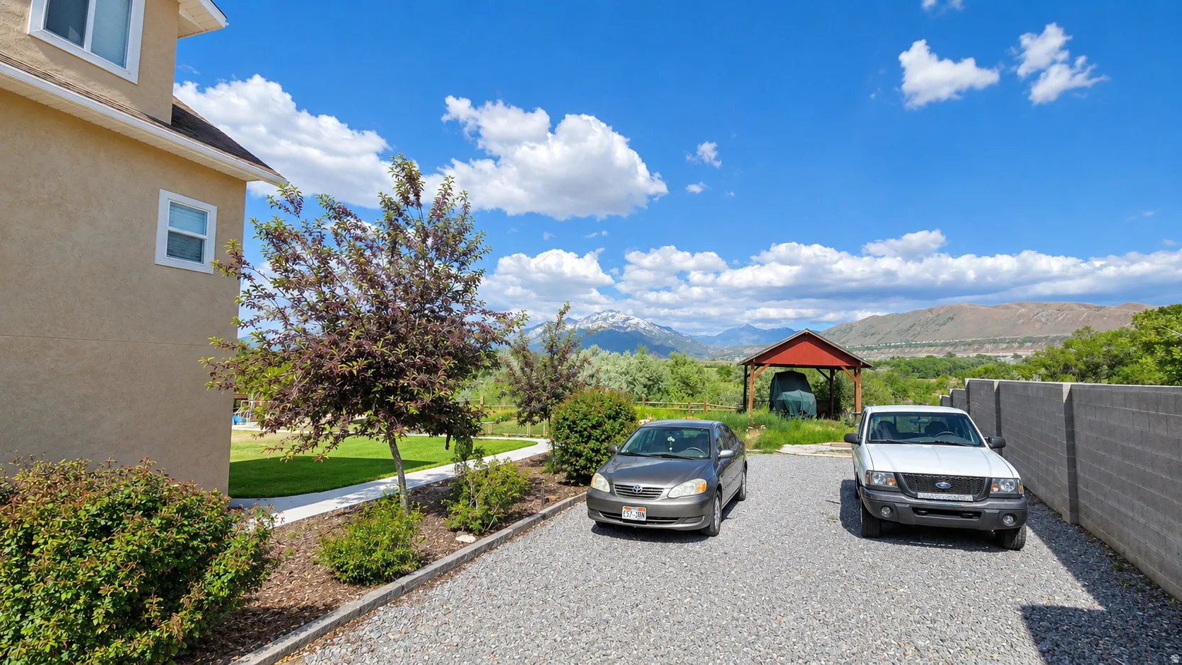 Gravel driveway alongside a stucco exterior, featuring a distant mountain backdrop