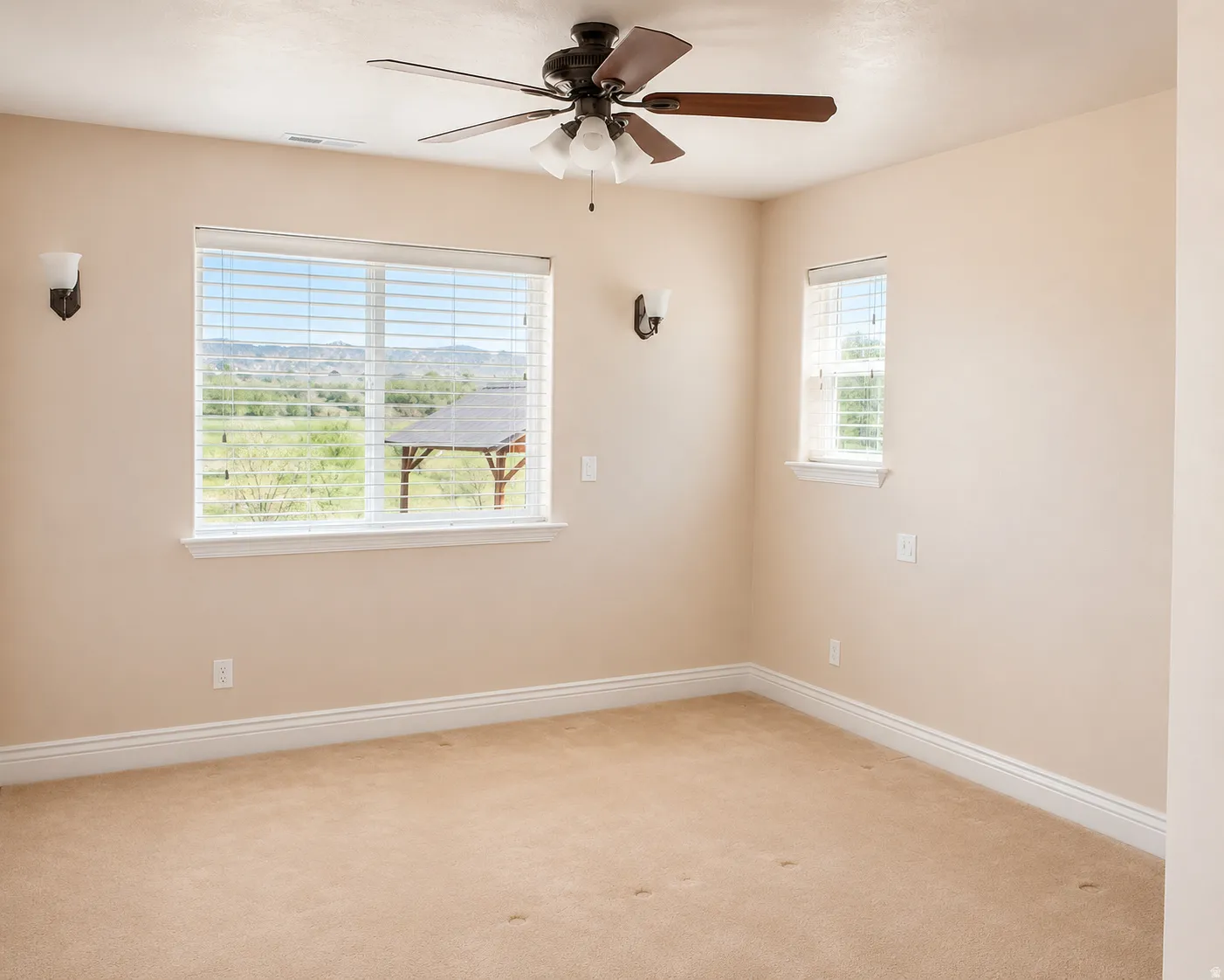ADU #2 - Spacious room featuring neutral carpeting, a ceiling fan with integrated lighting, and two windows equipped with horizontal blinds, offering expansive landscape scenery